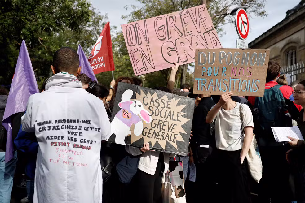 Manifestantes seguram cartazes enquanto se reúnem em frente ao hospital Tenon durante um dia de protestos em Paris, como parte de um movimento de protesto popular chamado 'Bloquons Tout' ('Vamos Bloquear Tudo')
